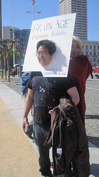 A man cosplaying as a Brain Age: Express Sudoku game box.